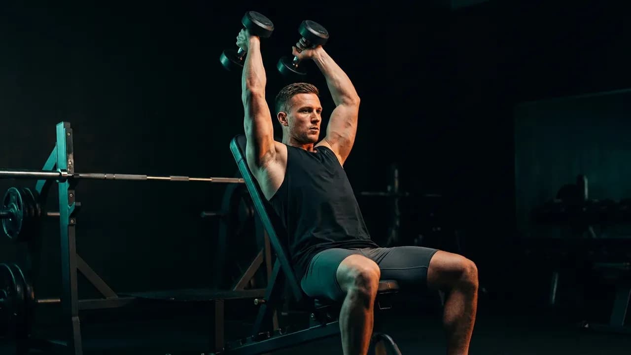an athlete performing overhead dumbbell triceps extensions on an incline bench angled at 60 degrees