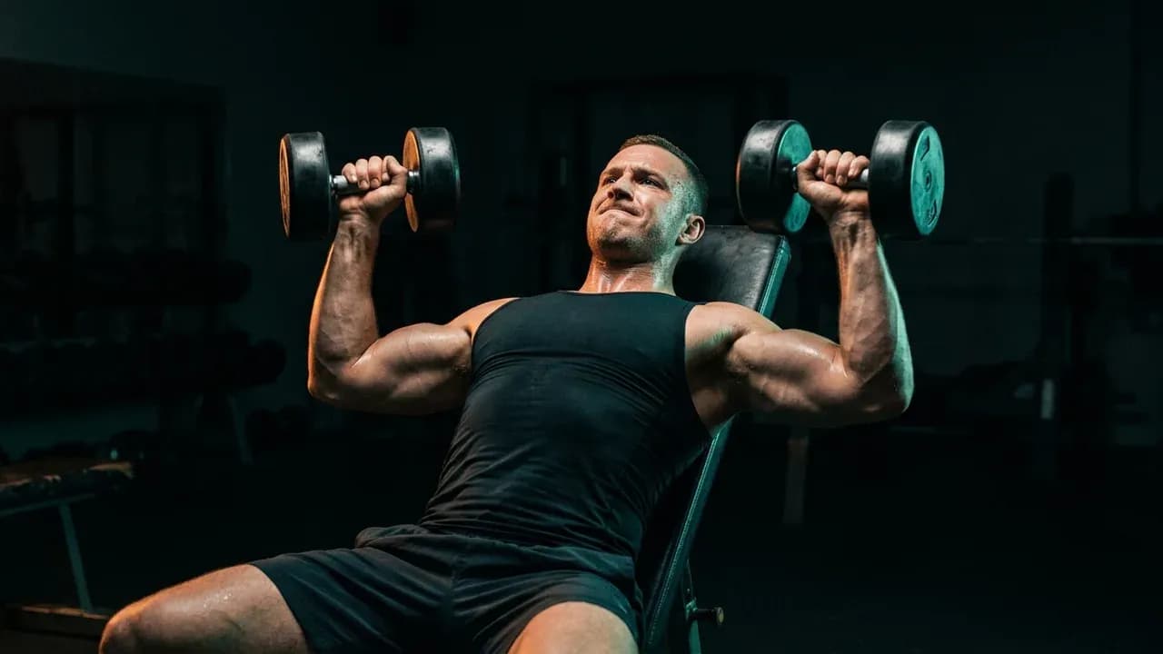 an athlete in a dimly lit gym performing a dumbbell incline press with intense concentration