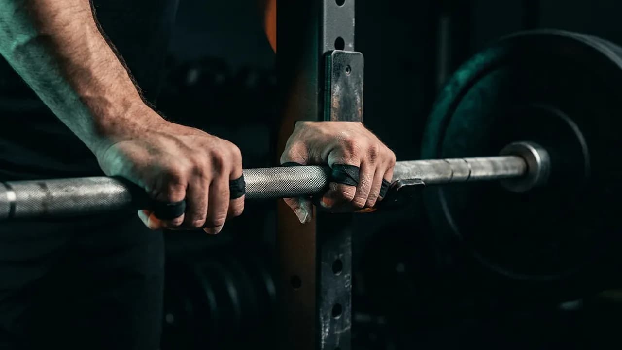 Close-up of hands gripping a knurled barbell resting on a squat rack before a lift